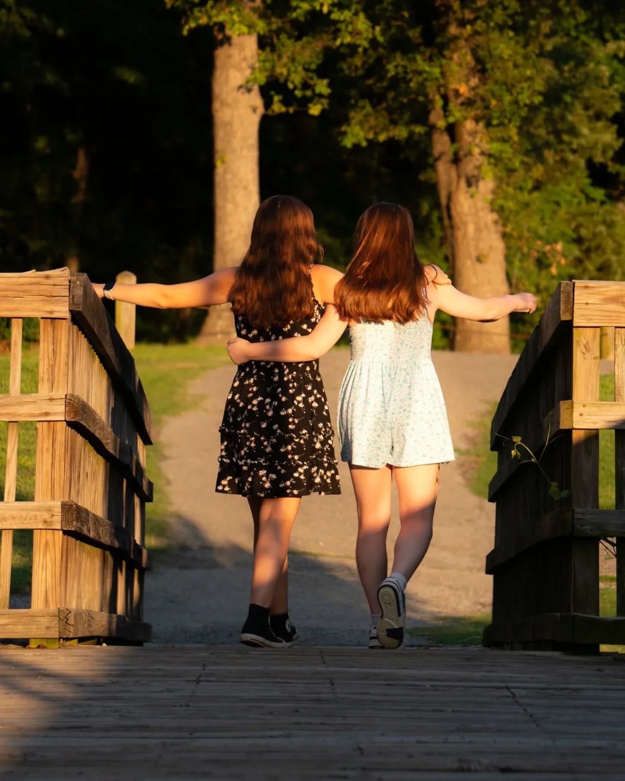 Two people walking together across a wooden bridge in golden evening light